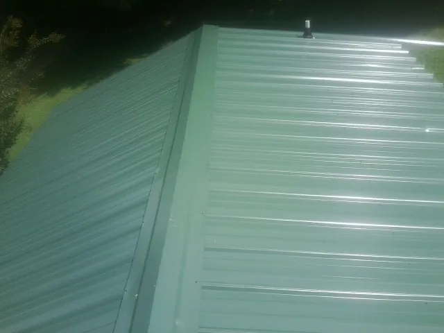 New green metal panels meeting at the ridge of a roof — Flat Roof Repair work by our crew in Snyder